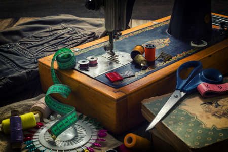 Old sewing machine and accessories for sewing, scissors, needles and tailor tape on the table. The concept of sewing accessories. Retro toningの写真素材