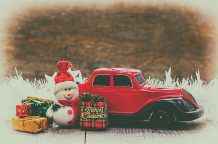 Christmas present, red miniature car with a snowman and gifts on a wooden surface. Christmas holiday concept. Card. Free space for text, retro styleの写真素材