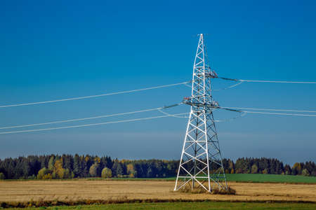 High voltage overhead power lines in a rural landscape against a blue sky with clouds.