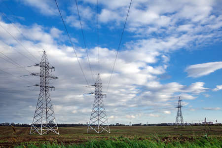 High voltage overhead power lines in a rural landscape against a blue sky with clouds.