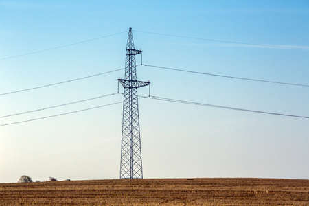 High voltage overhead power lines in a rural landscape against a blue sky with clouds.の写真素材