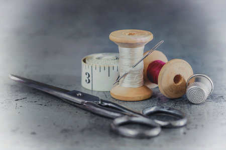 Multicolored threads on a wooden spool, sewing needle with scissors thimble and tailor's tape on an...