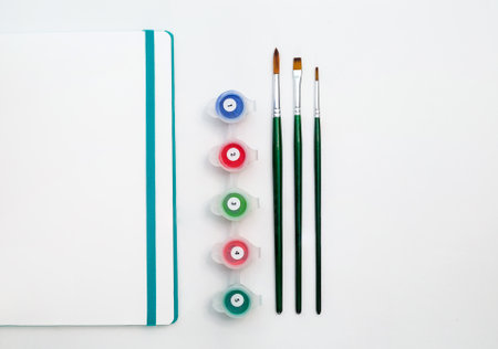 Notepad with paints of different colors and a brush on a white background. Drawing pad. With space for textの写真素材