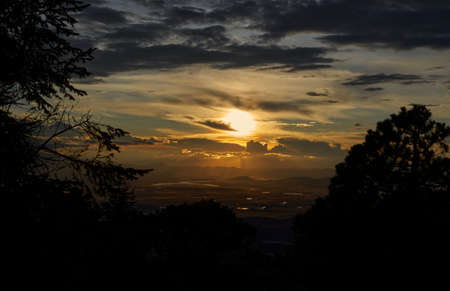 sun setting over the horizon at dusk with a dramatic sky of intense colorsの写真素材