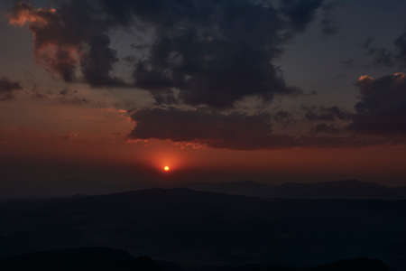 sun setting over the horizon at dusk with a dramatic sky of intense colorsの写真素材