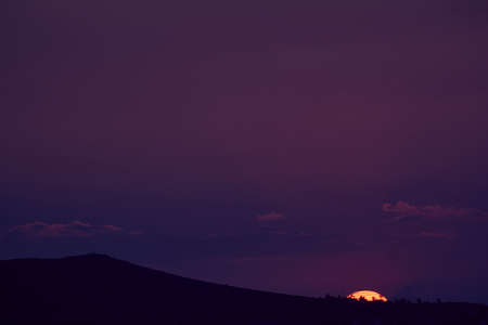 sun setting over the horizon at dusk with a dramatic sky of intense colorsの写真素材