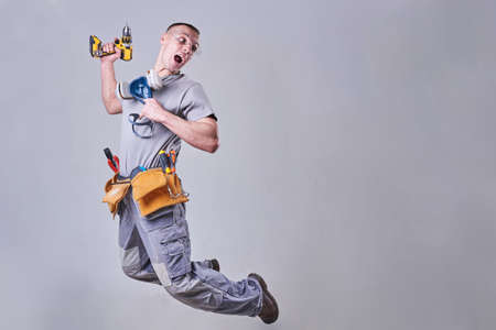 Master Builder-finisher in work clothes, with a drill-screwdriver jumping in his hands for any purposeの写真素材