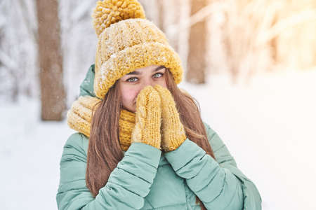 A beautiful young girl in a knitted hat warms her hands in winter, for any purposeの写真素材