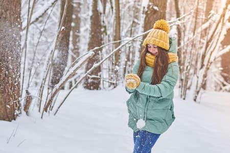 Beautiful young girl in a knitted hat,playing in the snow in forest for any purposeの写真素材
