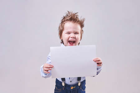 The little boy holds in hand a blank sheet of paper for any purposeの写真素材