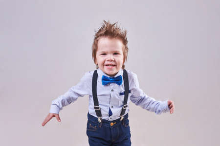 The little boy runs and smiles, wearing a blue bow tie and suspenders, for any purposeの写真素材