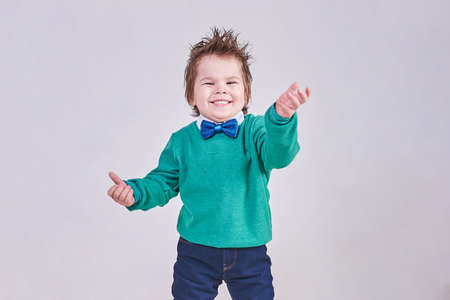 A handsome little boy, wearing a blue bow tie and a green sweater, dances and smiles for any purpose