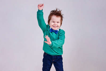 A handsome little boy, wearing a blue bow tie and a green sweater, dances and smiles for any purposeの写真素材