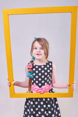 Beautiful little girl, with a funny expression on his face, holding a yellow frame for any purpose