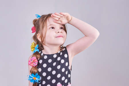 A beautiful little girl looks up, putting her hand to her forehead, for any purpose