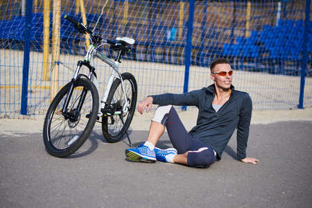 Sports man sitting next to the bike for any purposeの写真素材