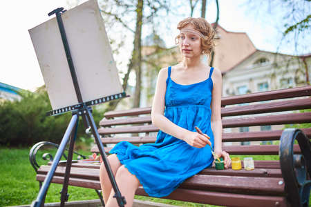 Beautiful girl-artist on the street in a blue dress, draws on the easel for any purposeの写真素材