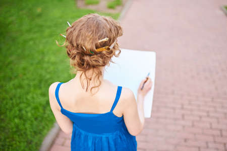 Beautiful girl-artist on the street in a blue dress draws a sketch of the picture for any purpose