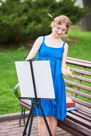 Beautiful girl-artist on the street in a blue dress, draws on the easel for any purposeの写真素材