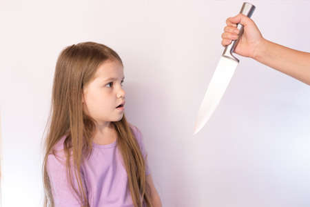 The little girl, frightened looks on the knife that it swung on a light background for any purposeの写真素材
