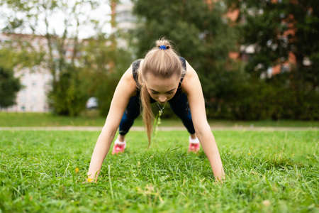 Beautiful athletic girl showing an exercise plank on the grass. For any purpose