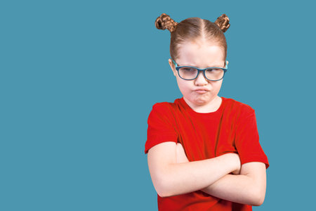 little girl with glasses offended. Isolated on a blue background. For any purpose.の写真素材