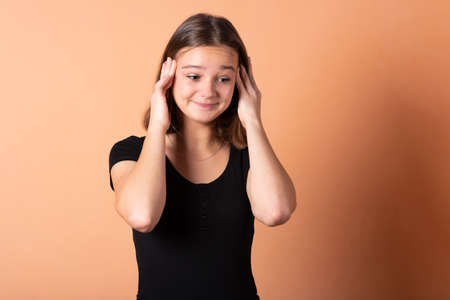 The girl is worried and holds on to her head, on a light orange background. For any purpose.の写真素材
