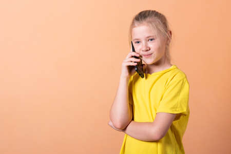 Little girl with a smartphone on a light orange background. For any purpose.