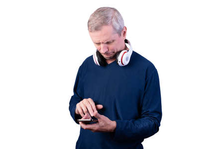 An elderly man is using a telephone. With wireless headphones on the neck. Isolated on a white...