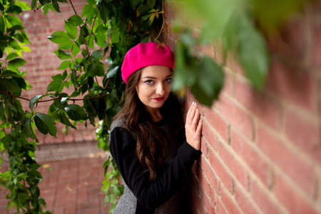 A girl in a pink beret is standing near a brick wall. For any purpose.の写真素材