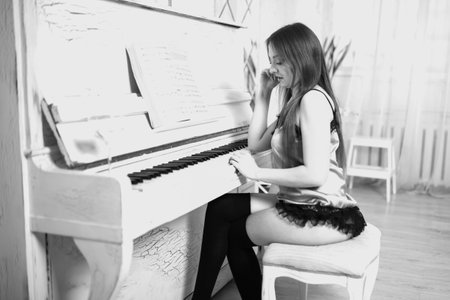 Attractive girl, in lingerie and stockings, sits at the piano and looks at the keys. For any purpose.の写真素材