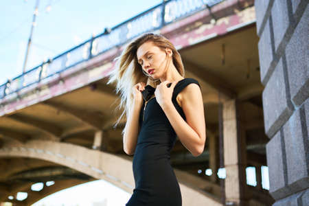 Sexy blonde girl in a black dress. Against the background of an arched bridge. For any purpose.