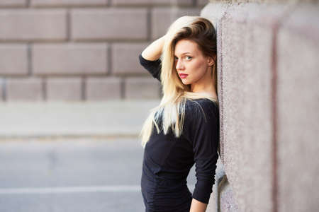 Beautiful blonde girl with red lipstick. Straightens hair. Against the background of a stone wall. For any purpose.の写真素材