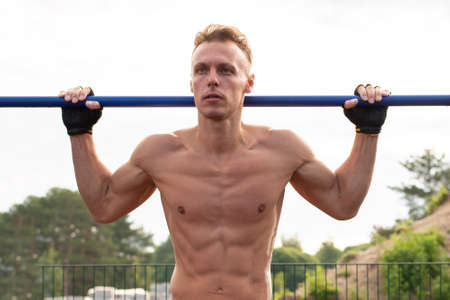 Muscular man pulls himself up on the crossbar. In the open air. For any purpose.