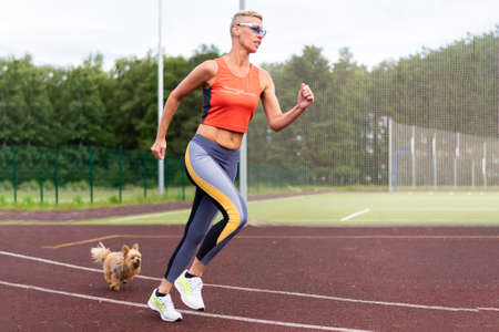 An adult woman runs in the stadium, with a little dog. For any purpose.
