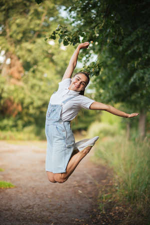 The girl in overalls jumps with legs crossed.の写真素材