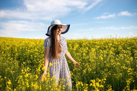 Beautiful girl in a hat and dress, in a rapeseed field, against the sky. High quality photoの写真素材