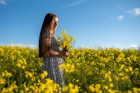 Beautiful girl in a rapeseed field, with a bouquet in her hands against a blue sky. High quality...