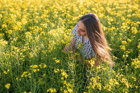 A girl in a canola field, with her hair loose, sniffs canola. High quality photo