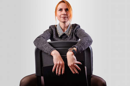 Business woman, legs wide apart, sits on a chair backwards, on a gray backgroundの写真素材