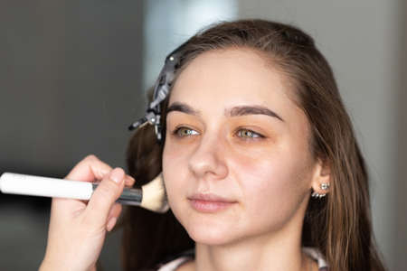 Makeup artist distributes foundation on the girl's face with a brush. high quality photo