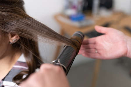 The stylist curls the girl's hair with a curling iron. high quality photoの写真素材