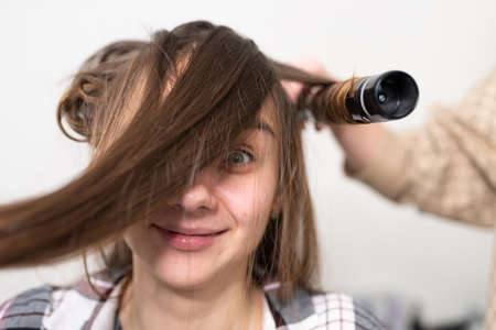 The stylist curls the girl's hair with a curling iron. high quality photoの写真素材