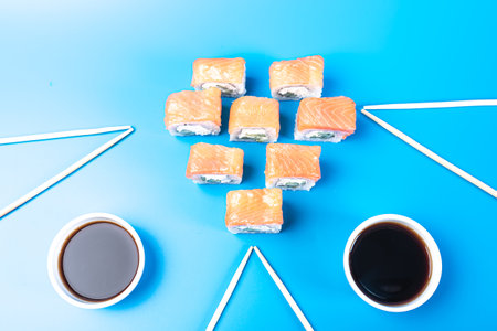 Sushi rolls with salmon, cheese and cucumber, with soy sauce in a bowl, on a blue background. high quality photoの写真素材