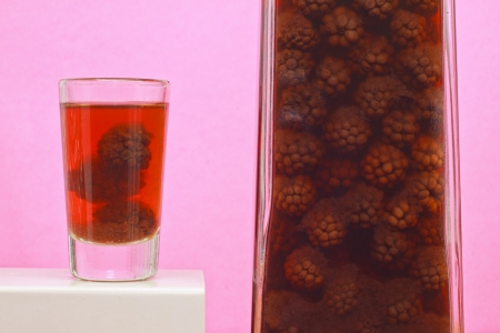 Bottle and one shot of homemade blackberries liqueur on white wooden table and pink backgroundの写真素材