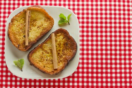 Spanish Torrijas and two cinnamon pieces on a red and white tableclothの写真素材
