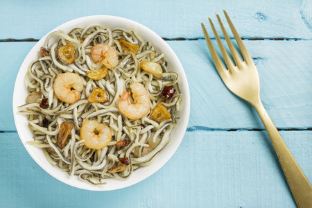 Surimi elvers with prawns, garlic and pepper on a white bowl, golden fork on a blue wooden tableの写真素材