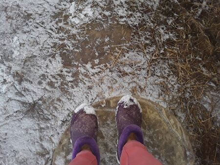 Female legs and boots on a background of snowy ground and grass