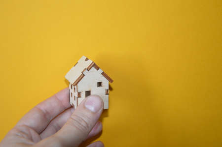 Small wooden house in a man's hand on a the yellow backgroundの写真素材