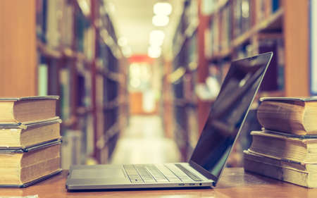 Educational e-learning class and e-book digital technology concept with pc computer notebook open in blur school library or classroom background among old stacks of book, textbook archive collectionの写真素材